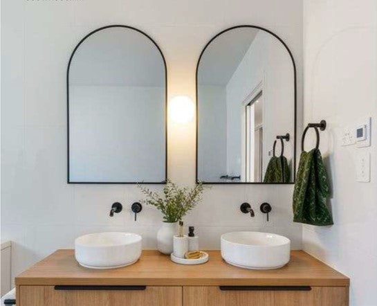 Bathroom vanity with two round sinks, wooden countertop, and two arched mirrors.