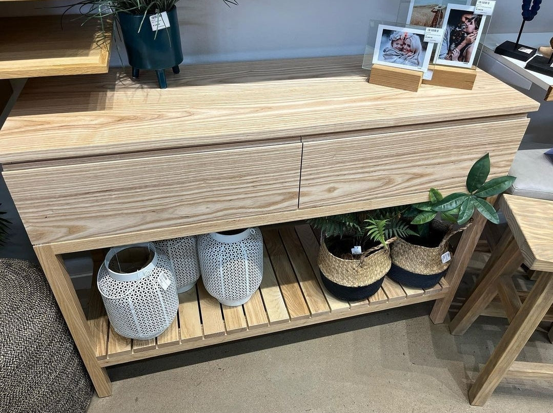 A solid wood server unit with drawers, displayed in a furniture store setting, with decorative items on top.