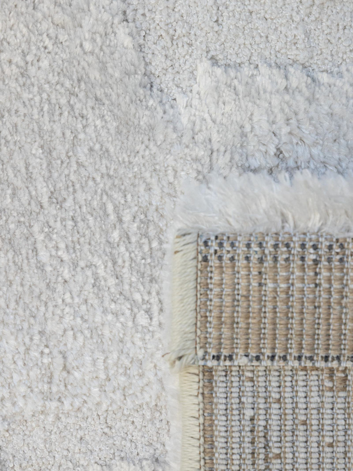 Close-up of a textured off-white shag rug with a woven beige and white corner showing cream fringe.
