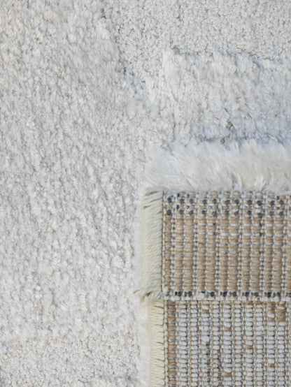Close-up of a textured off-white shag rug with a woven beige and white corner showing cream fringe.
