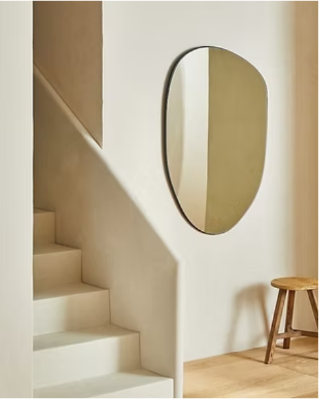 Round mirror on a wall next to a staircase in a minimalistic interior.